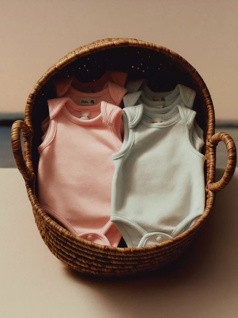 Stak af babybodyer og blød sovedragt i pasteller i kurv